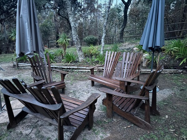 A patio area with wooden Adirondack chairs and a small table, surrounded by a garden with various plants and a wooden fence. - Lovely 3 bed Troutbeck Cottage - 2295 (Nyanga)