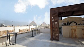 A rooftop terrace with a seating area, a bar, and a view of pyramids in the distance.