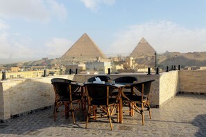 A rooftop terrace with a table and chairs, a view of the pyramids, and a stone wall. - Pearl pyramids Inn (Giza)
