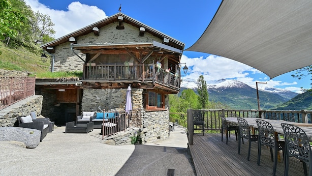 A chalet with a balcony, outdoor seating, and a mountain view.