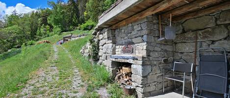 A stone building with a wooden roof, a fireplace, and a metal chair.