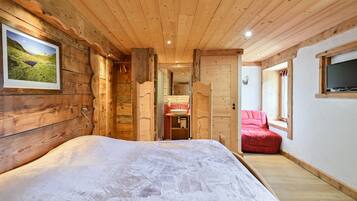 A wooden cabin interior with a bed, a red chair, a TV, and a bathroom with a sink.