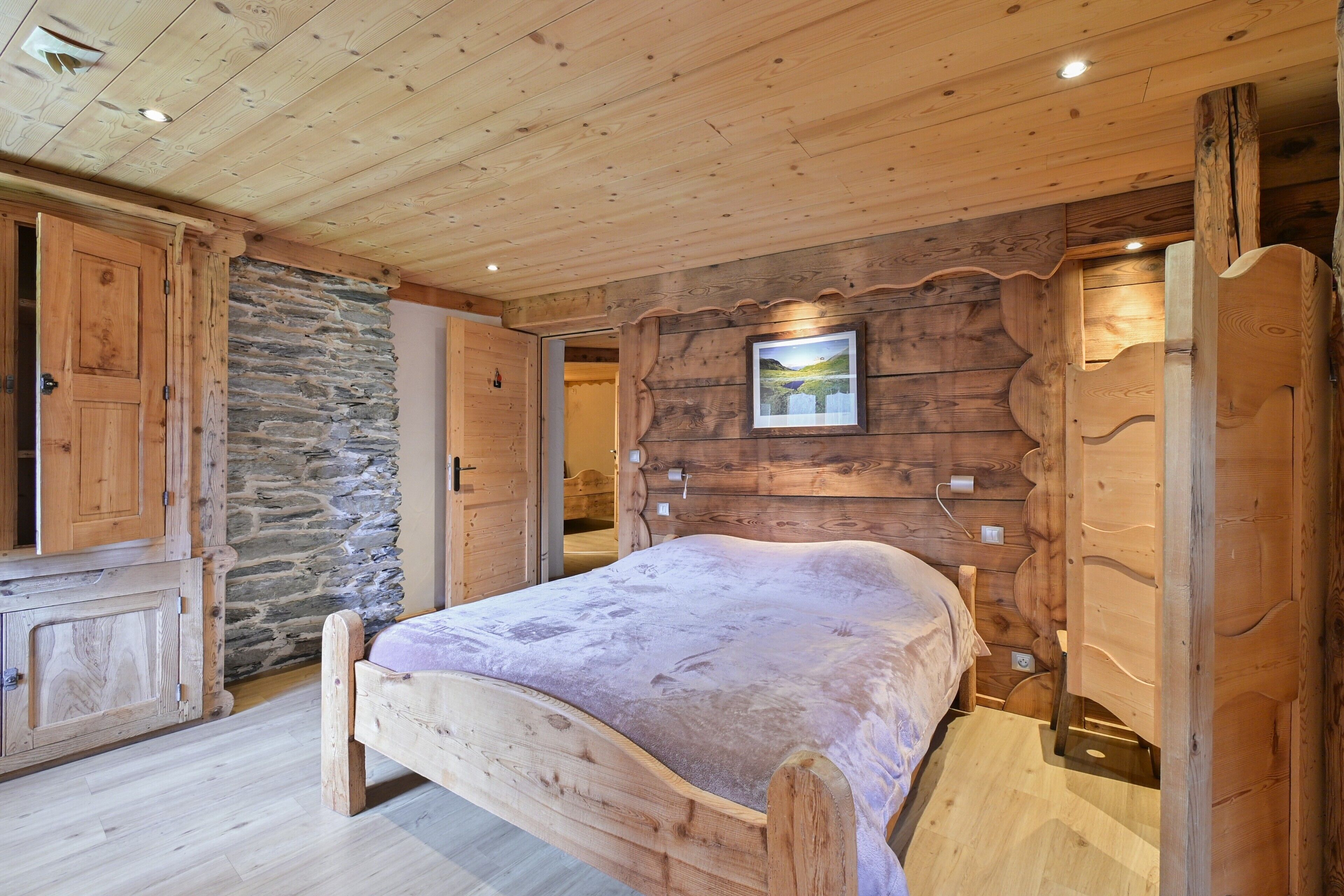 A wooden bedroom with a bed, stone wall, and wooden cabinets.