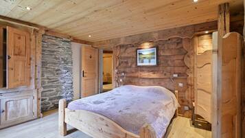 A wooden bedroom with a bed, stone wall, and wooden cabinets.