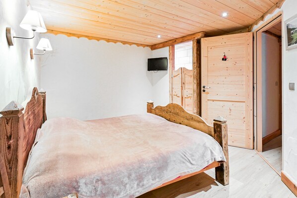 Un dormitorio con una cama de madera, un televisor montado en la pared y una puerta de madera.