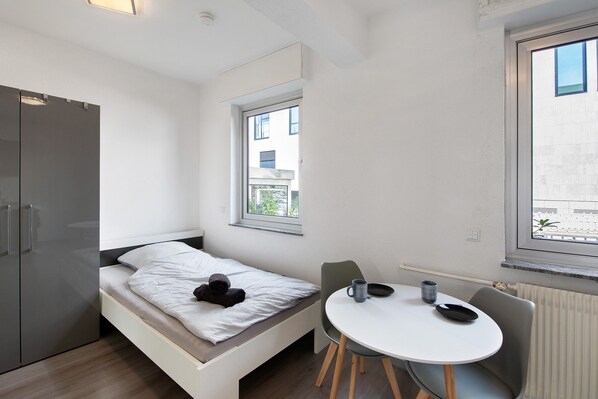 A small, modern room with a bed, a table, and a window.