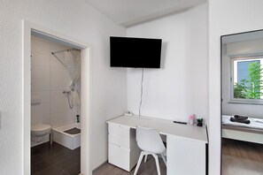 A modern bathroom with a shower, toilet, and a white vanity with a flat-screen TV mounted above.