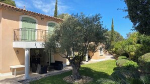 Una villa de estilo mediterráneo con balcón, un jardín cuidado y un cielo azul despejado.