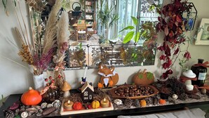 Ein Zimmer mit großem Fenster, einem Holztisch mit Dekoration und verschiedenen Pflanzen und Blumen.