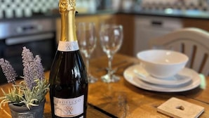 A bottle of Prosecco on a wooden table with a potted lavender plant, wine glasses, and a white bowl. - Traditional Country Cottage (Stanton Drew)