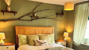 A neatly made bed with a wooden headboard, two bedside tables with lamps, and a branch decoration on the wall. - Traditional Country Cottage (Stanton Drew)
