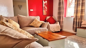 A living room with a beige sofa set, a wooden coffee table, and a red accent wall. - Traditional Country Cottage (Stanton Drew)