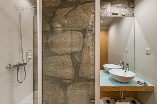A bathroom with a stone wall, a shower, and two sinks. - Guestready - Porto de Rio Residences (Porto)