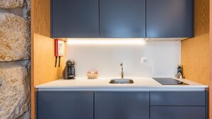 Une cuisine avec des meubles de couleur sombre, un plan de travail blanc, une machine à café, un évier et une bouteille d’eau.