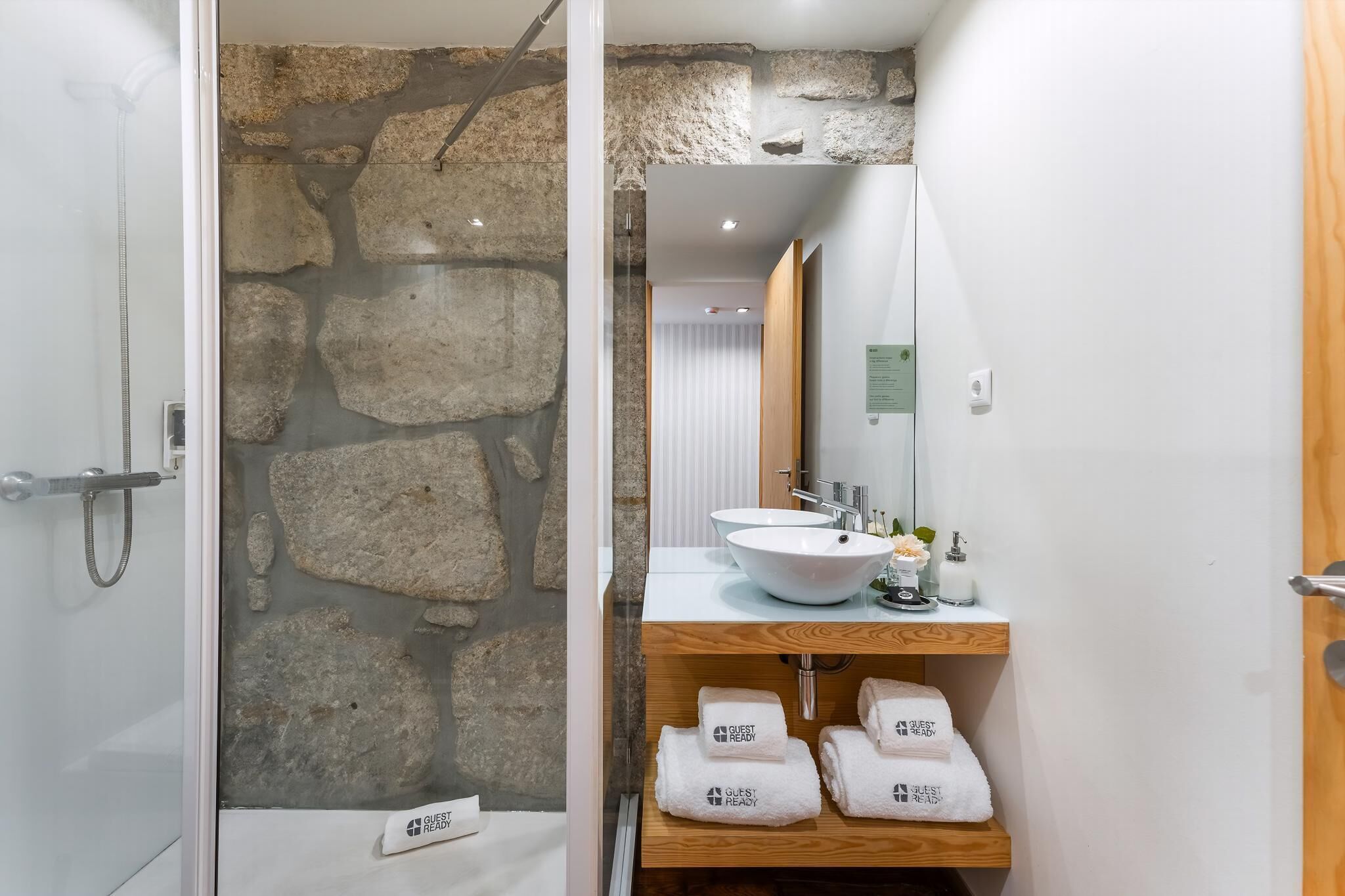 Une salle de bain avec un mur en pierre, un lavabo blanc, un miroir et un porte-serviettes avec des serviettes.