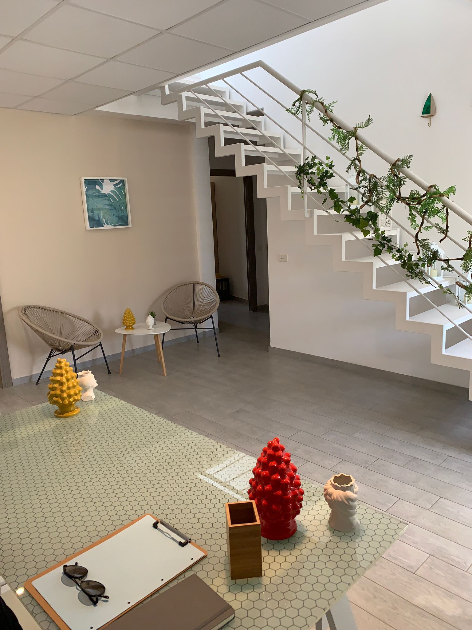 Ein modernes Interieur mit einer Treppe, zwei Stühlen, einem kleinen Tisch und dekorativen Elementen auf einem gemusterten Boden.