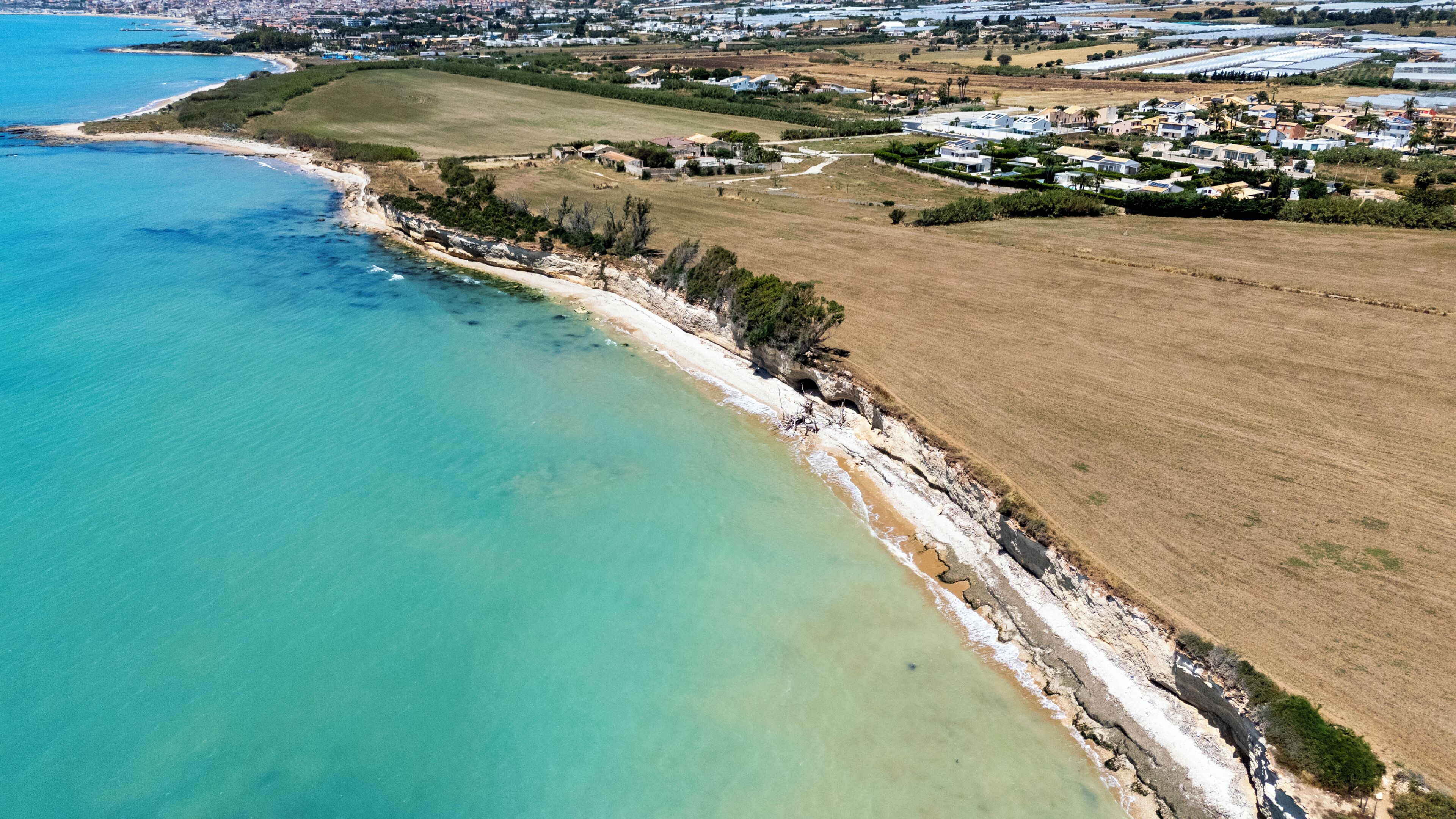 Vista aérea de una zona costera con playa, edificios residenciales y campos agrícolas.