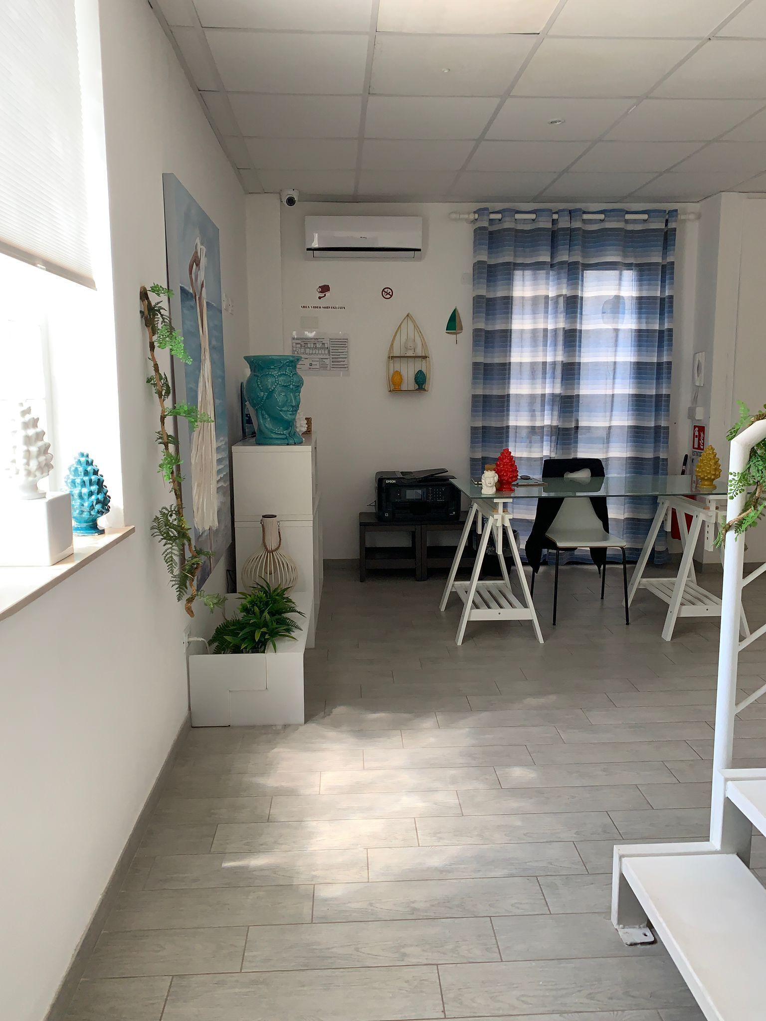 Un espace de bureau moderne avec un bureau blanc, un ordinateur et une chaise. Il y a une fenêtre avec des stores, une plante et un vase décoratif sur le bureau.