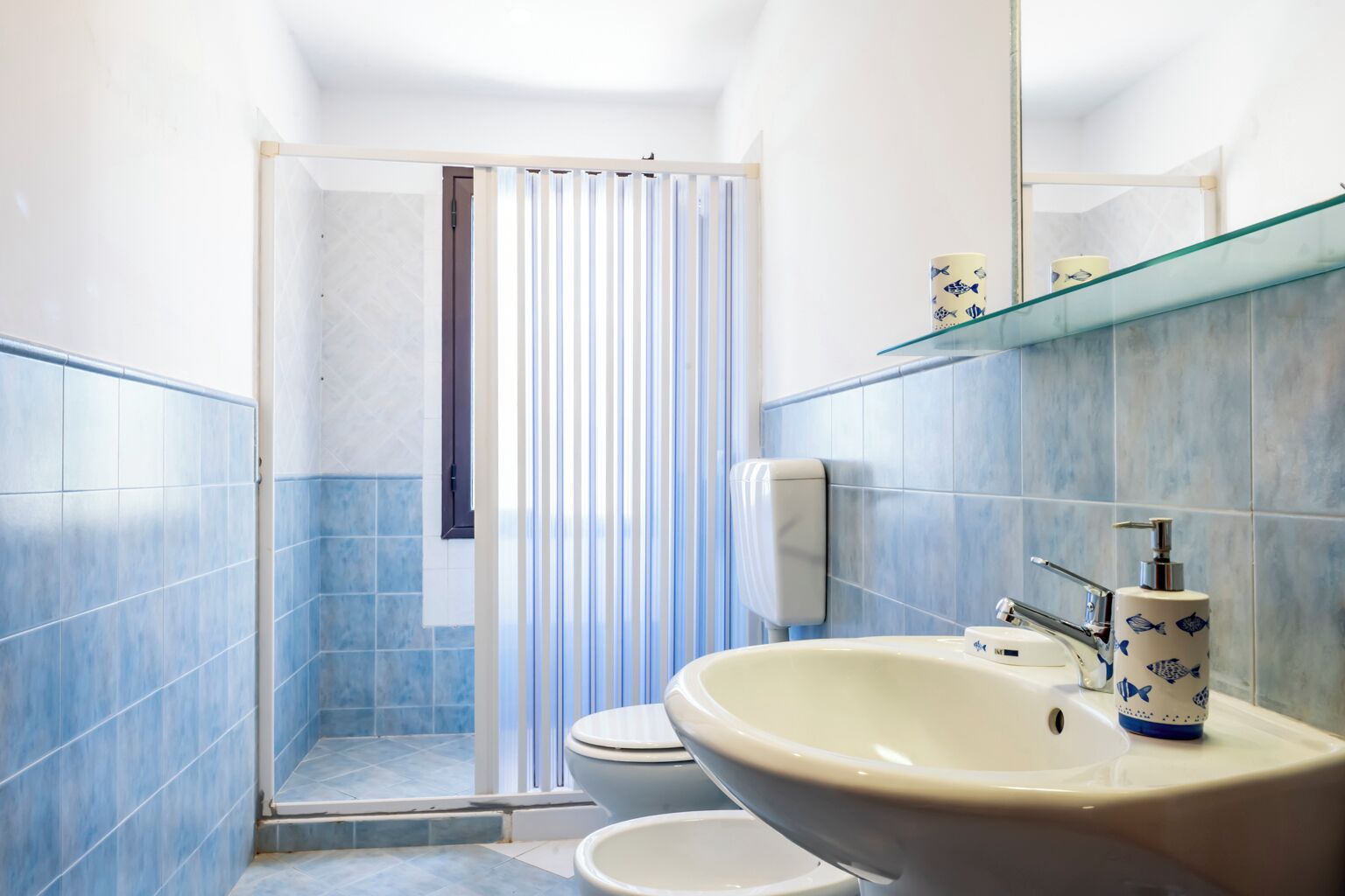 A bathroom with a shower, toilet, sink, and a glass shelf with toiletries.