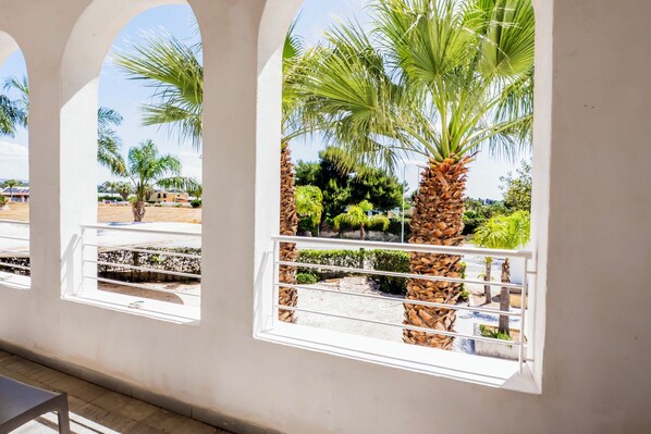 A building with arched windows overlooking a garden with palm trees and other greenery.