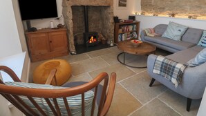 A cozy living room with a stone fireplace, a television, a bookshelf, and a comfortable sofa. - Sea Holly (Penzance)