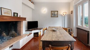 A dining area with a wooden table, chairs, a fireplace, a television, and a window with a view. - Holiday Home 'Casa Bellini' with Private Garden, Wi-Fi and Air Conditioning (Solarolo)