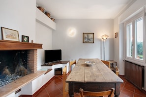 A dining area with a wooden table, chairs, a fireplace, a television, and a window with a view.