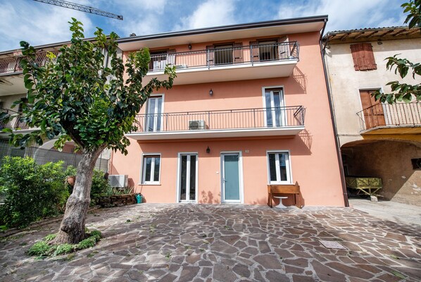 Un immeuble à plusieurs étages doté de balcons, d’une cour pavée de pierres et d’un arbre.