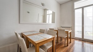 A dining area with a wooden table and chairs, a large mirror on the wall, and a sliding glass door leading to a balcony. - Guestready - Charming House Marquês (Porto)