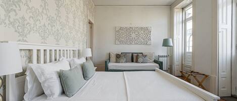 A bedroom with a large bed, a smaller bed, a chair, and a radiator.