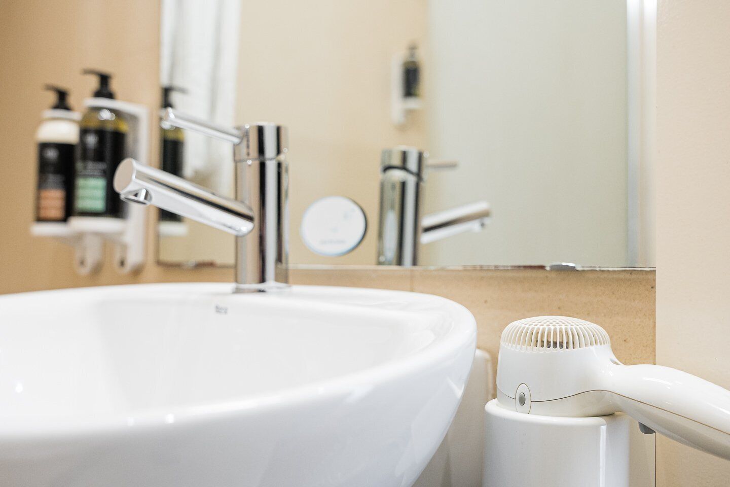 Baño con lavamanos blanco, grifo cromado y secador de pelo.