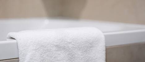 A white towel draped over a bathtub in a bathroom with beige tiles.