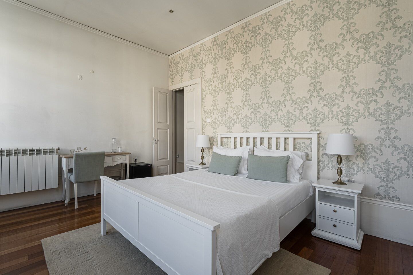 A bedroom with a bed, bedside tables, a desk, and a radiator.
