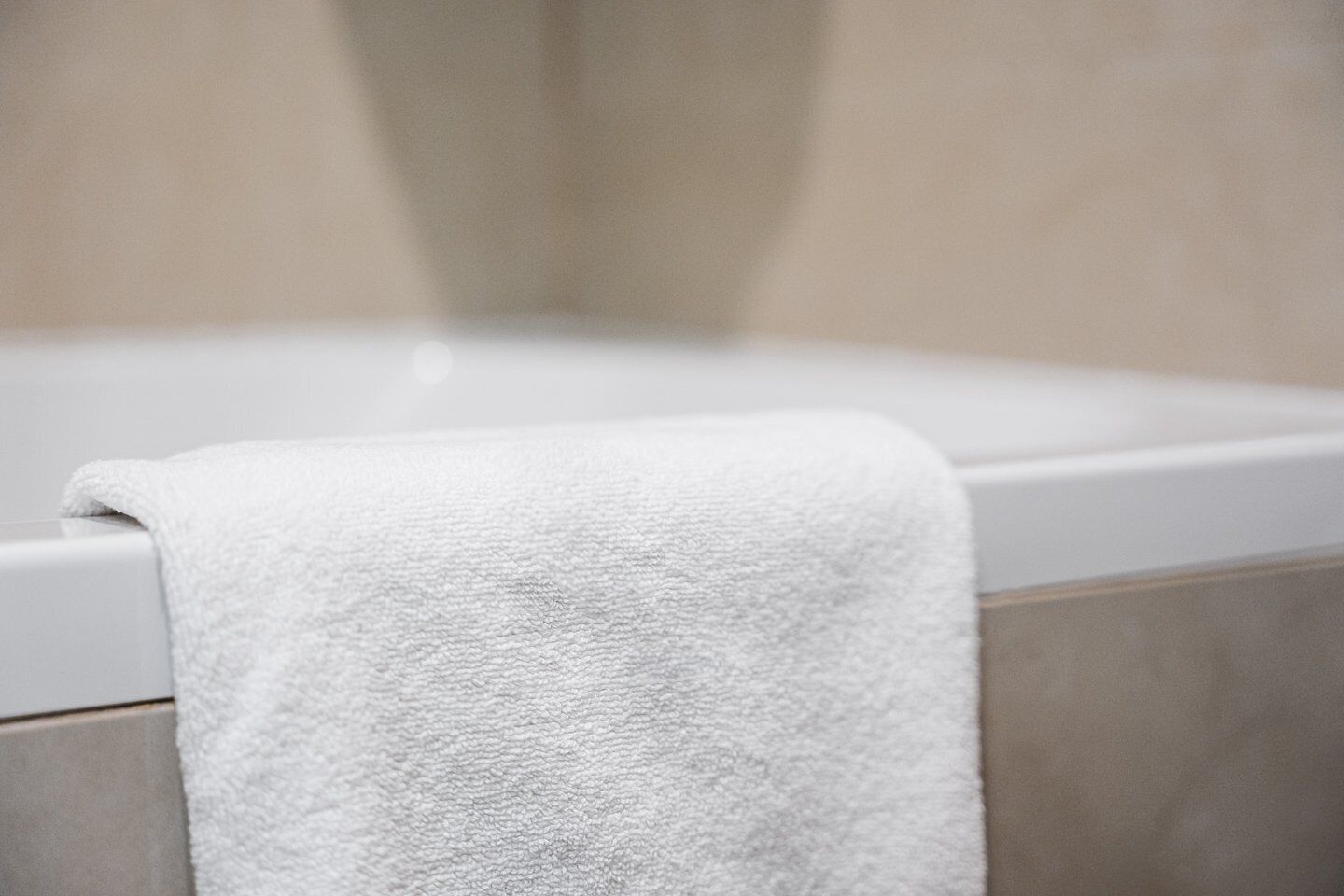 Een witte handdoek over een badkuip in een badkamer met beige tegels.