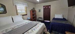 Une chambre avec deux lits, une armoire en bois, une fenêtre avec des rideaux en dentelle et une porte.