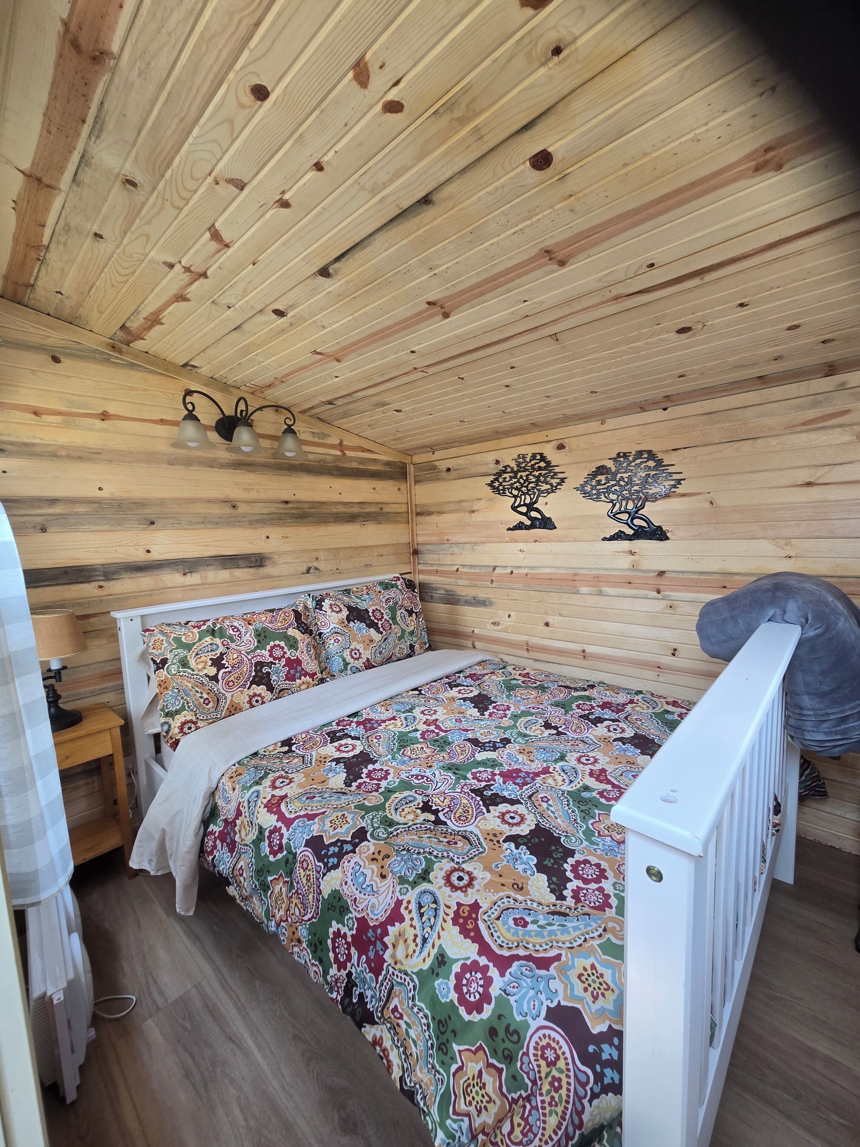 A wooden cabin room with a bed, a nightstand, and a wall-mounted lamp.