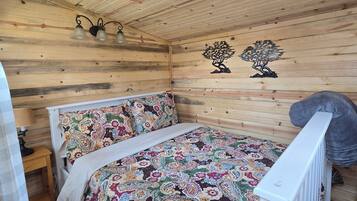 A wooden cabin room with a bed, a nightstand, and a wall-mounted lamp.