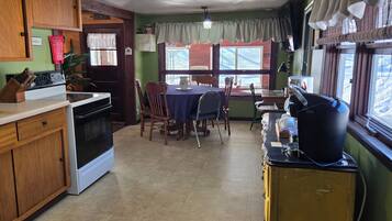 A kitchen with wooden cabinets, a stove, a dining table with chairs, and a window with a view.