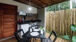 A compact kitchen with a microwave, kettle, and small refrigerator. There is a dining table with chairs and a small plant on it. - Itaka Studio Piscina Hidro e Quadra em Arraial (Porto Seguro)