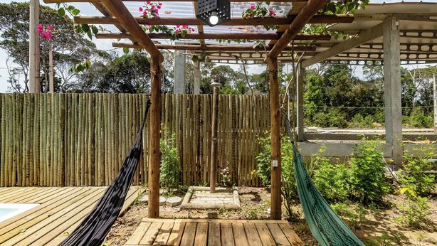 A wooden deck with a hammock, a pergola with climbing plants, and a bamboo fence. - Itaka Studio Piscina Hidro e Quadra em Arraial (Porto Seguro)