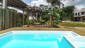 A swimming pool with a wooden deck, a hammock, and a pergola with climbing plants. - Itaka Studio Piscina Hidro e Quadra em Arraial (Porto Seguro)