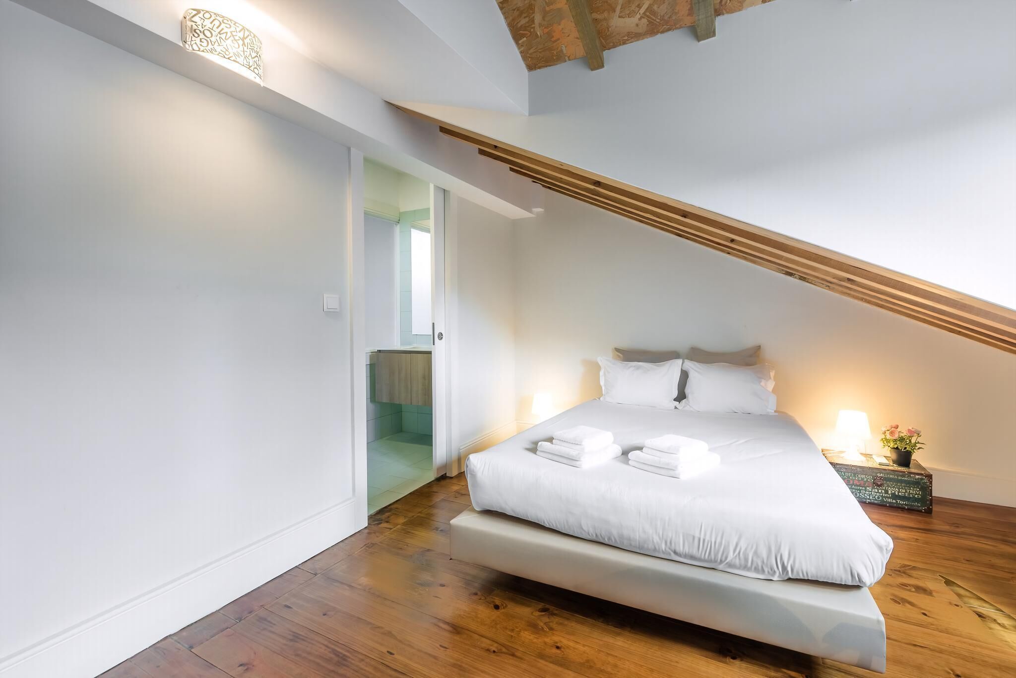 Et soveværelse med en stor seng, et sengebord med lampe, og udsigt til et badeværelse.