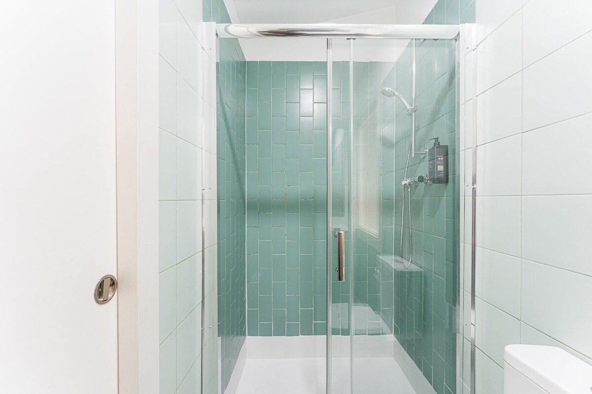 A glass-enclosed shower stall with a white toilet and a handheld showerhead.