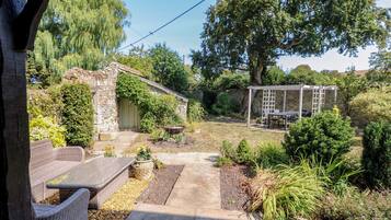 Un jardín rústico con un edificio de piedra, una pérgola y mobiliario de exterior.