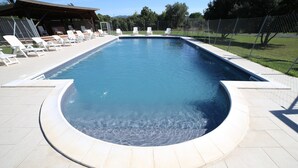 Una piscina rettangolare con bordo curvo, circondata da lettini bianchi e un'area relax coperta.