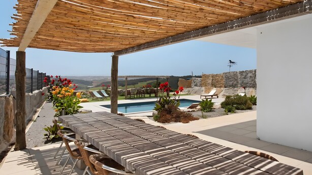 Un espacio de estar techado al aire libre con piscina, sillones de descanso y vistas al campo.