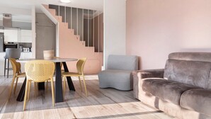 Un salon moderne avec un canapé gris, une table à manger entourée de chaises jaunes et un escalier menant à l’étage supérieur.
