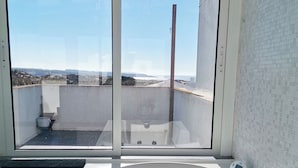 A bathroom with a large bathtub, a window with a view of the cityscape, and a tiled wall. - Sea View Terrace Wellness Apartment - Duna Parque Group (Odemira)