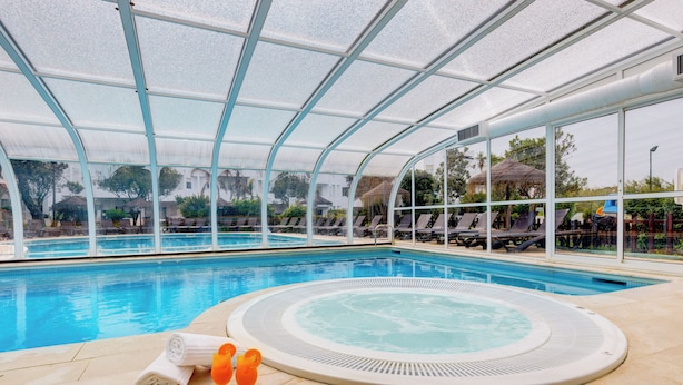 An indoor swimming pool with a hot tub, lounge chairs, and a glass-enclosed roof. - Sea View Terrace Wellness Apartment - Duna Parque Group (Odemira)