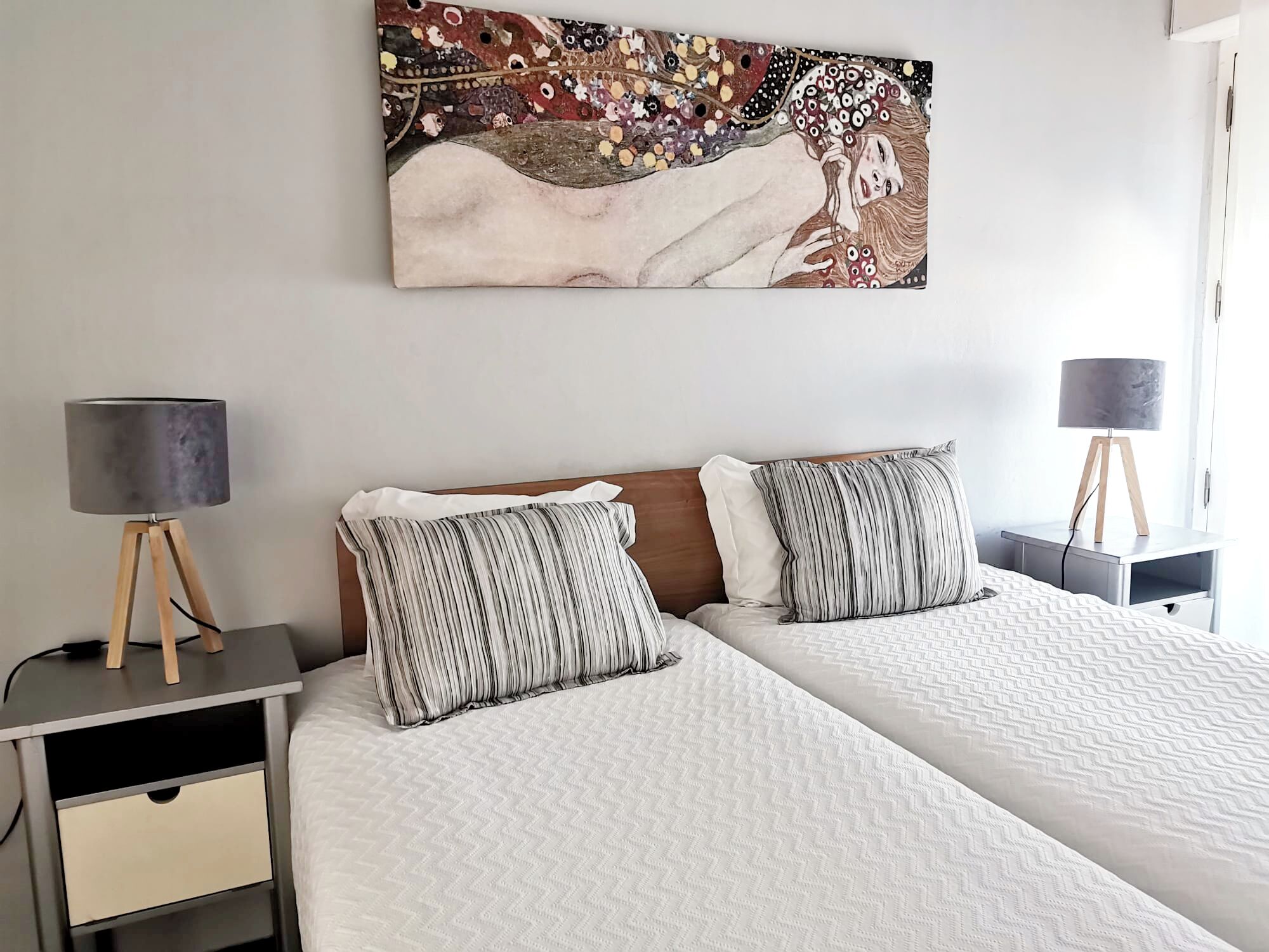 Ein Doppelbett mit gestreifter Bettwäsche, ein Nachttisch mit Lampe und ein Bild an der Wand.